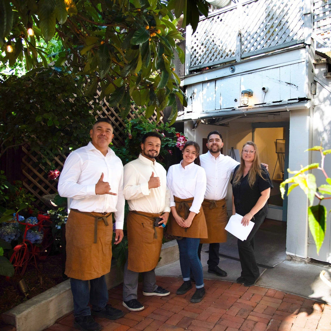 Group of people posing outdoors with a building and plants in the background