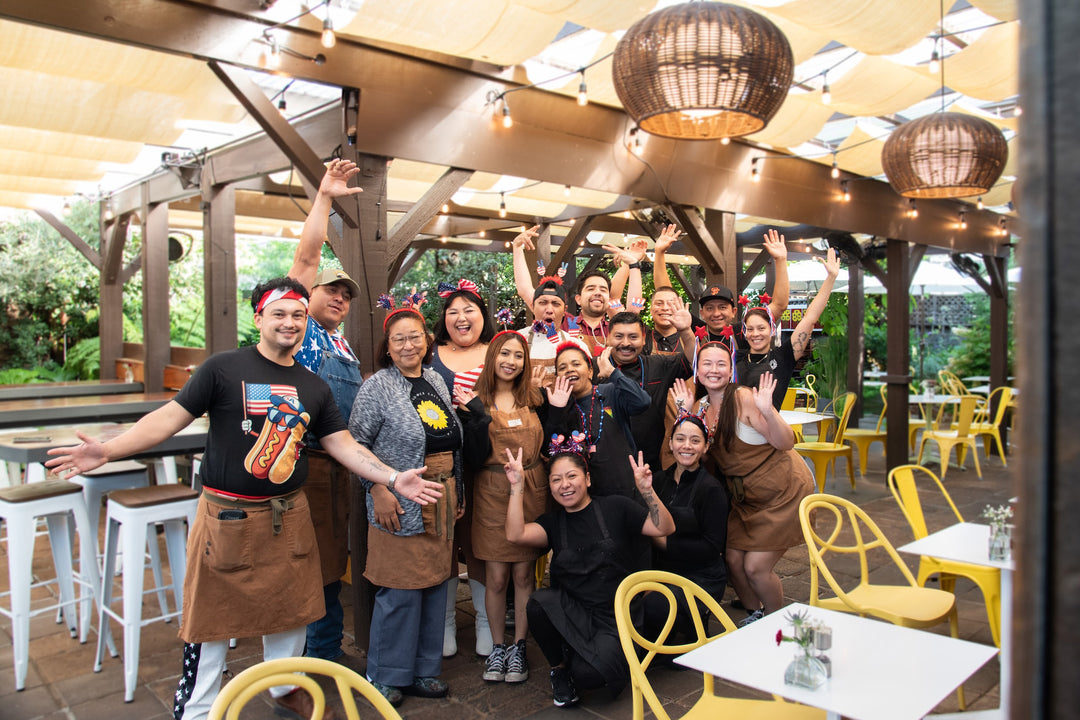 Group of people posing together in a restaurant setting with wooden beams and pendant lights.
