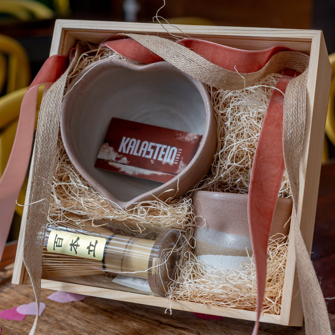 Gift set with a heart-shaped bowl, bottle, and box on a wooden surface with pink heart confetti.