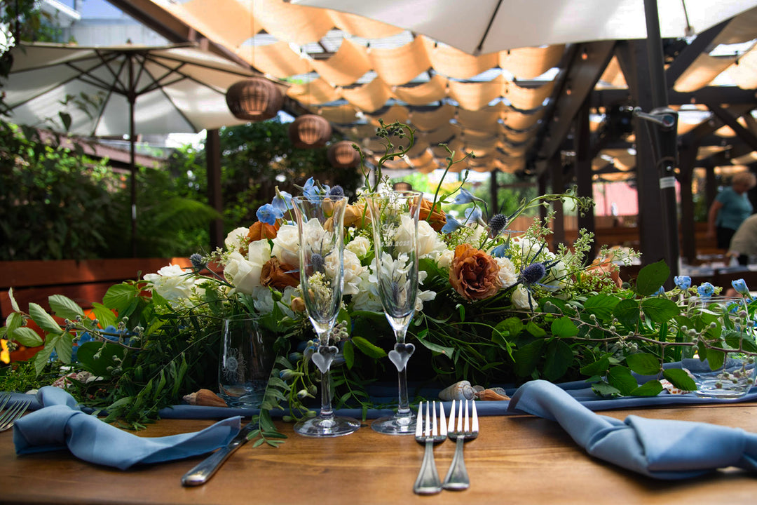 Decorated table with flowers, glasses, and cutlery under an outdoor canopy.