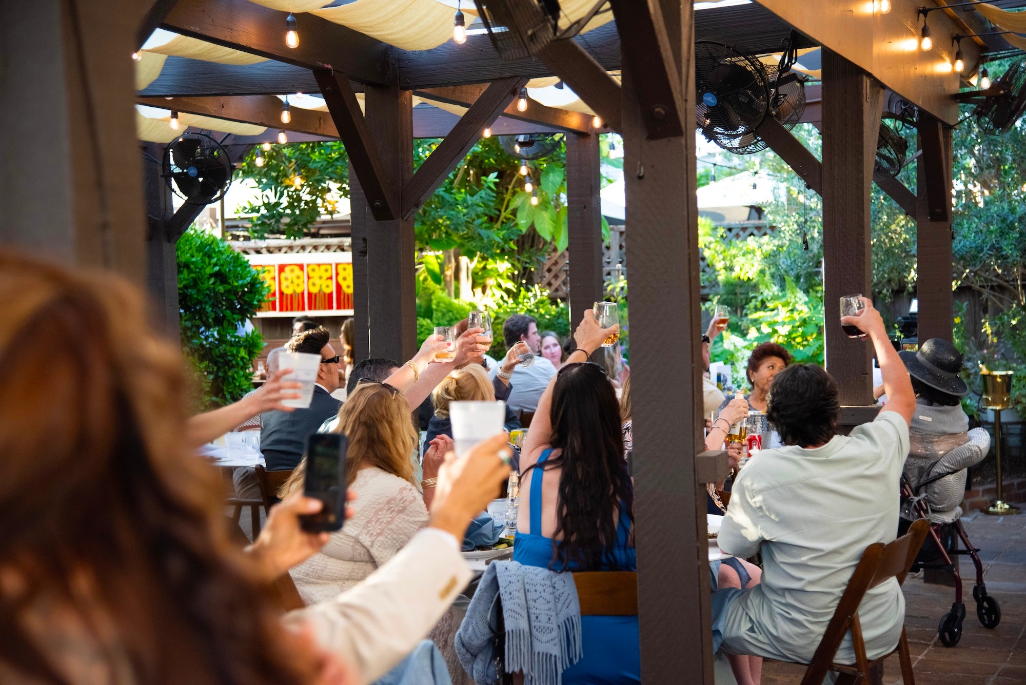 People sitting outdoors at a restaurant, raising their glasses in a toast.