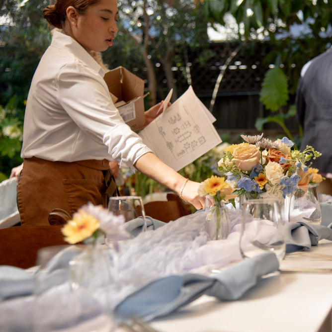 Person arranging flowers at a table outdoors