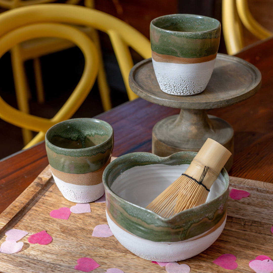 Ceramic tea set with two cups and a bowl on a wooden tray with pink heart decorations.