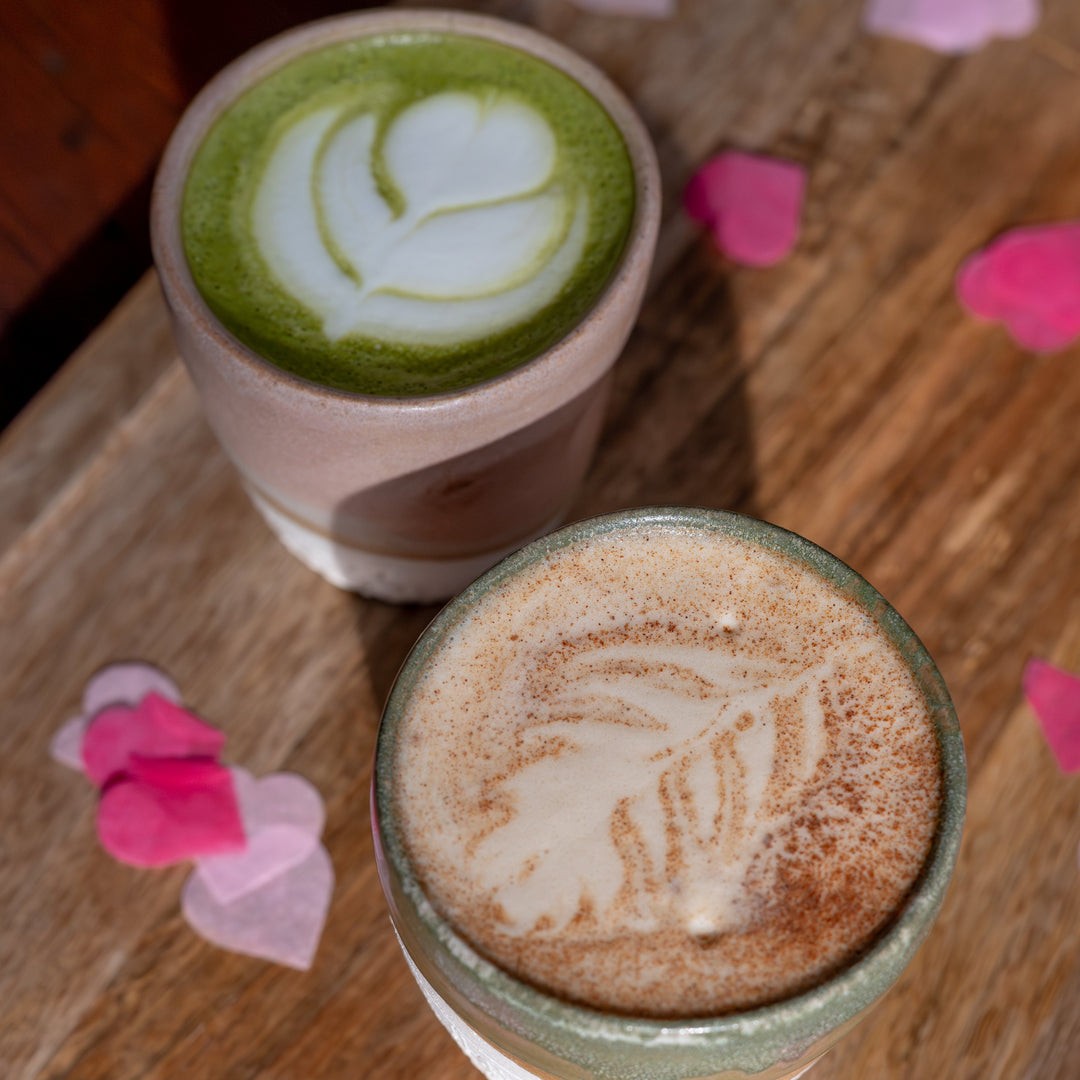 Two cups of coffee with latte art on a wooden surface with heart-shaped confetti.