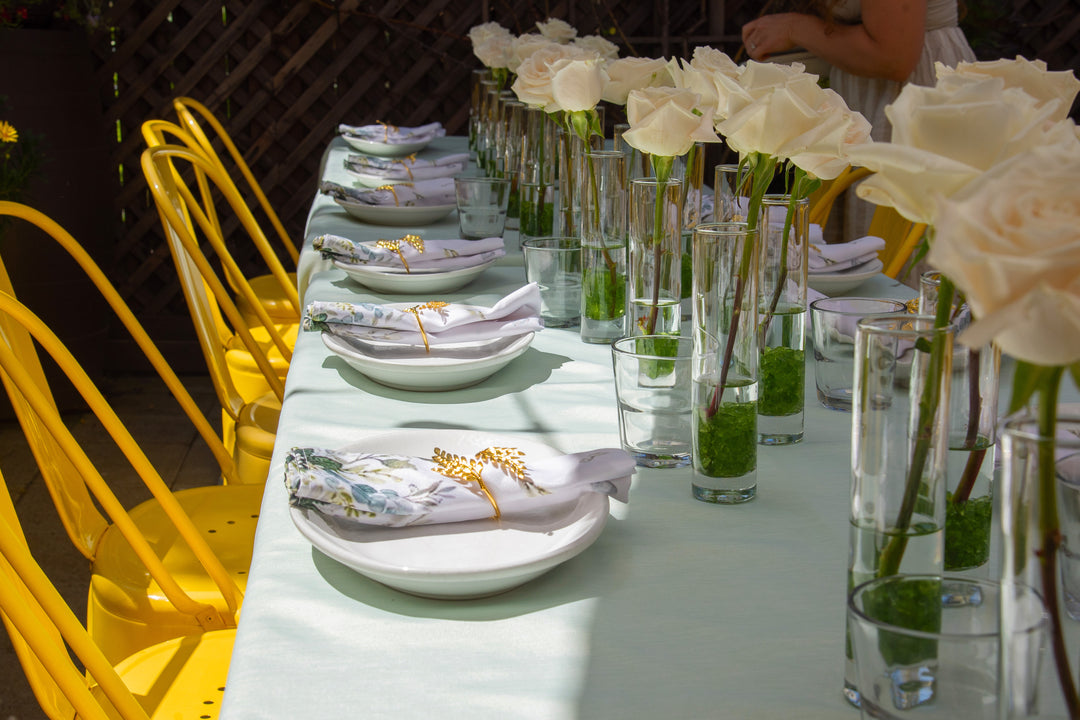 Dining table set with white roses, glasses, and decorative plates with yellow accents.
